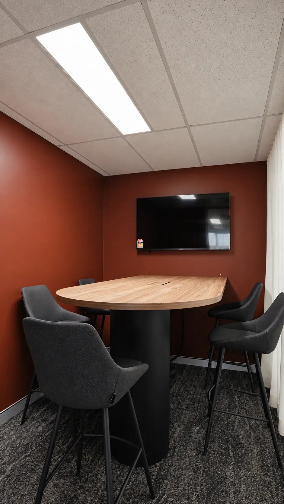 Small meeting room with a timber table, high chairs and a wall-mounted screen