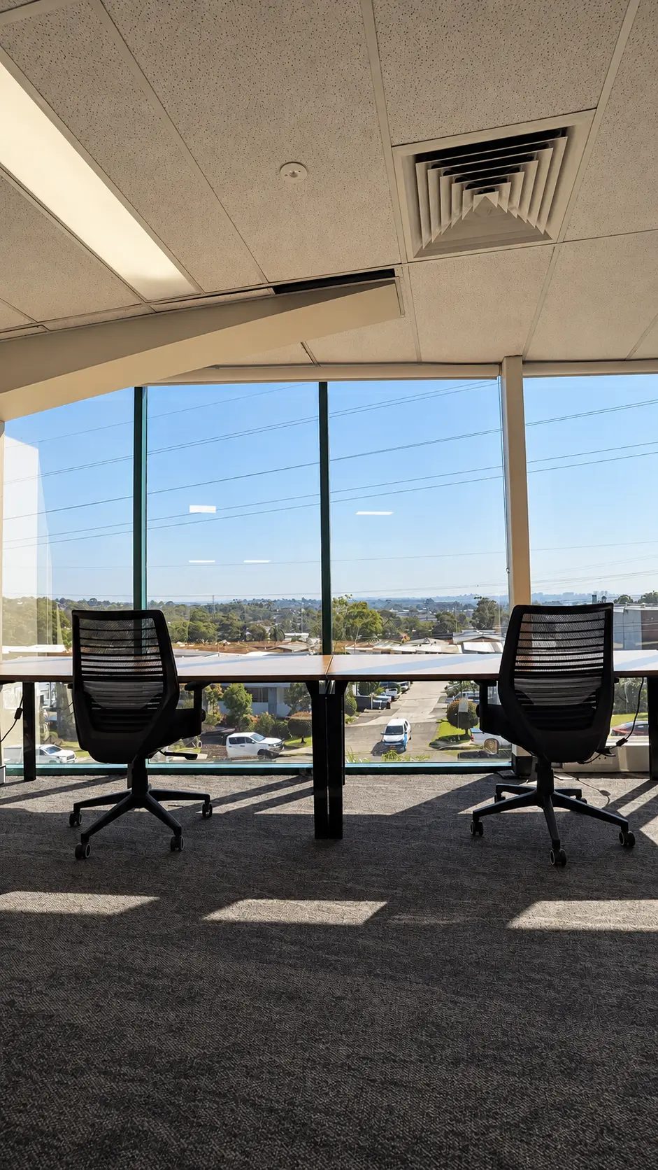 Desks and chairs beside floor-to-ceiling windows with a view over rooftops