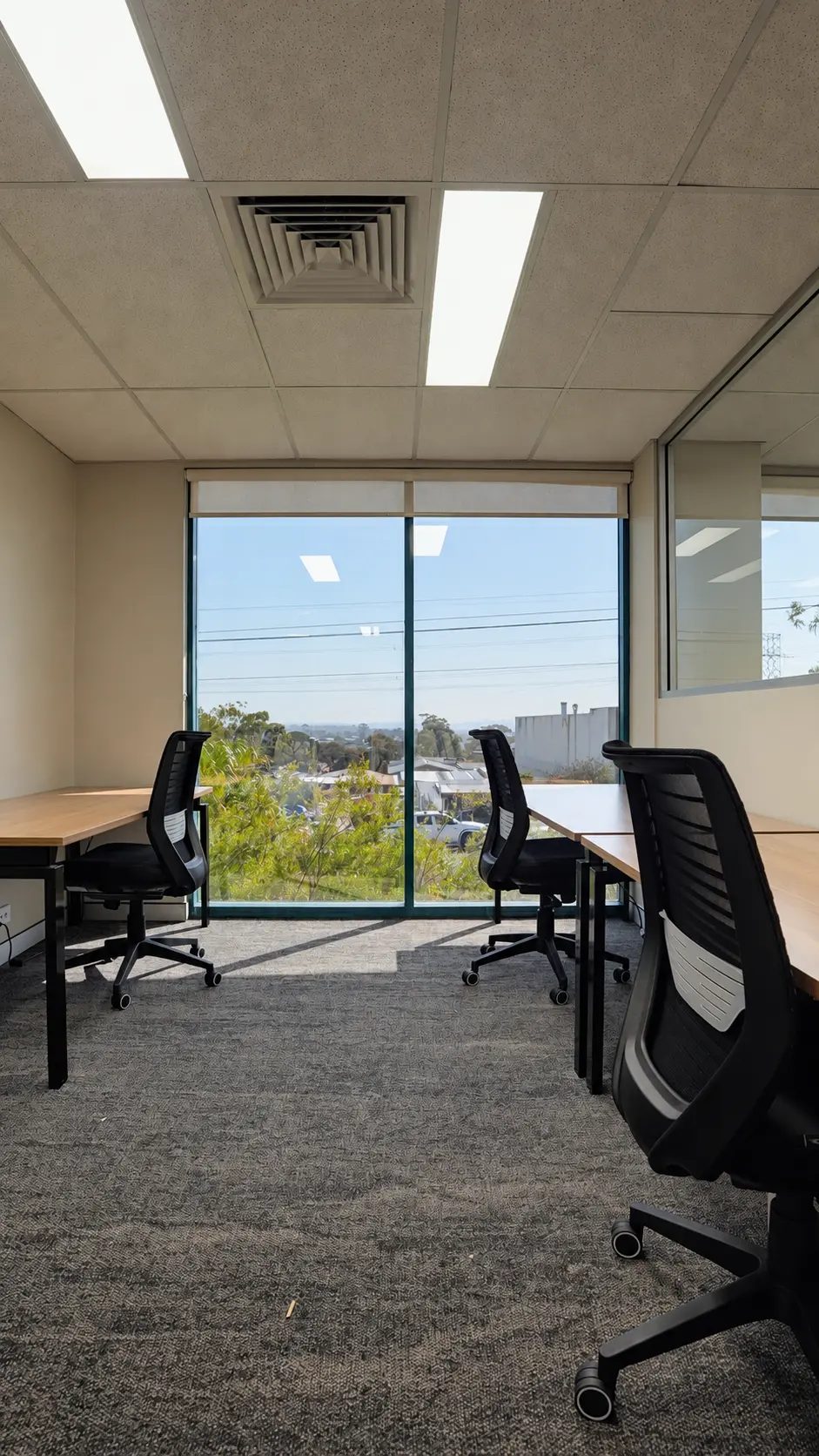 Office with desks, chairs and a large window overlooking trees and rooftops